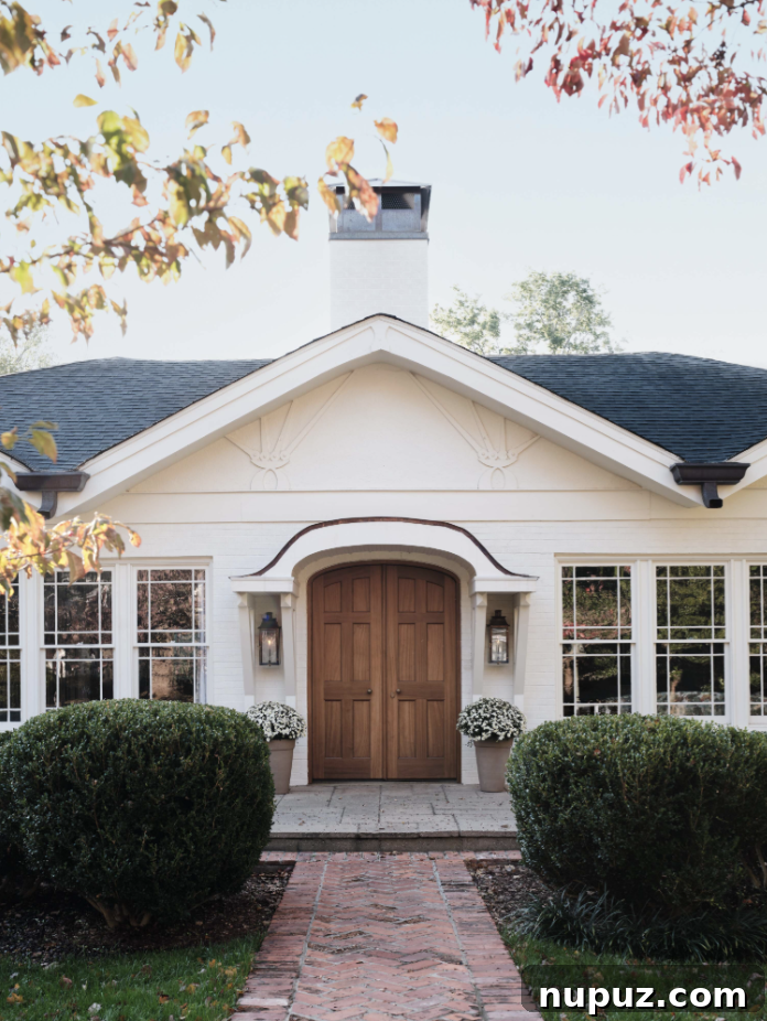 Elegant white exterior of a Catskills home designed by Stephanie Sabbe, featuring an inviting arched doorway and natural stone accents, beautifully captured by Joseph Bradshaw Photography.