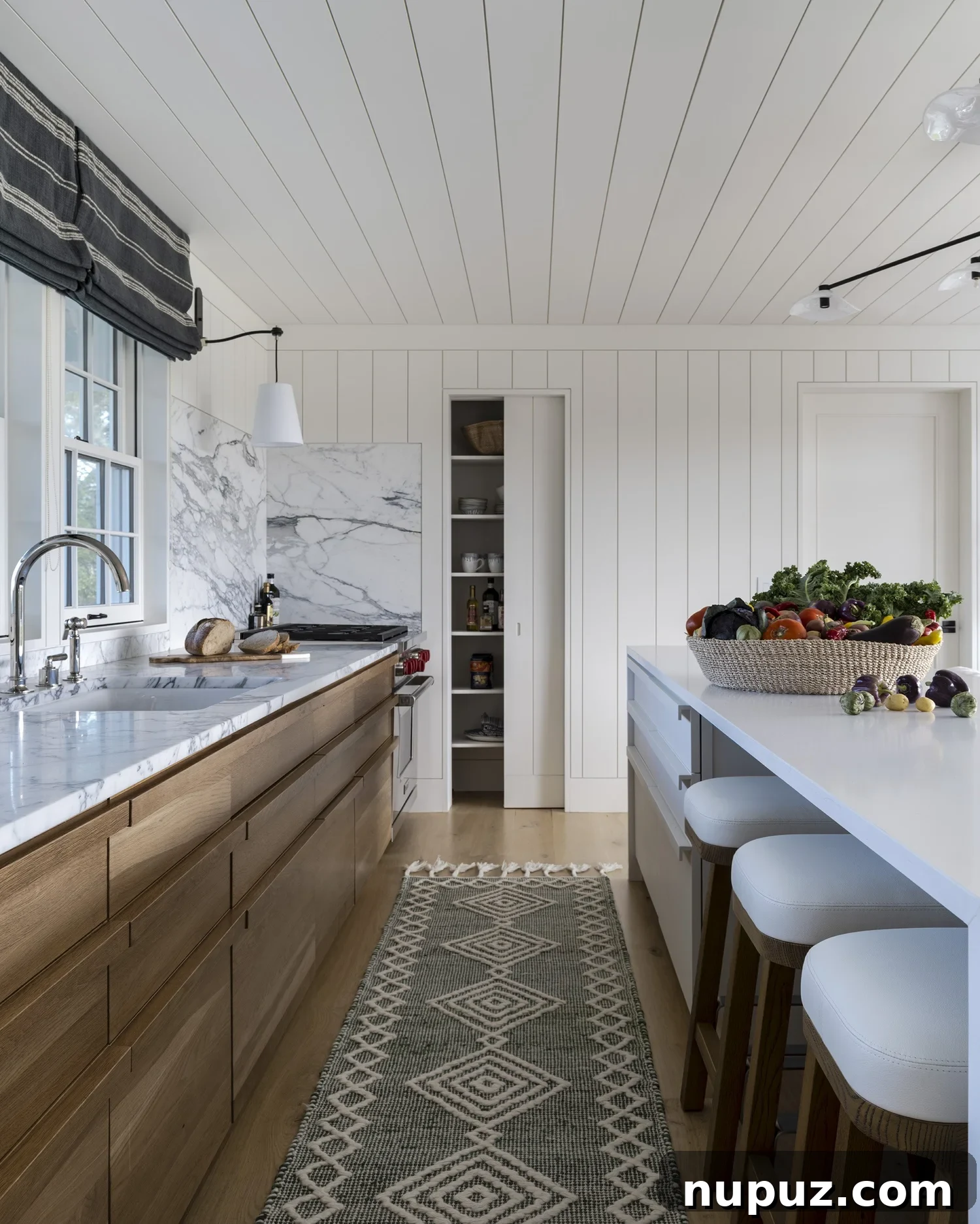 Nantucket's Timeless Coastal Sanctuary Unveiled 4 Stylish kitchen in Nantucket home with white cabinets, stained wood accents, and elegant marble countertops and backsplash
