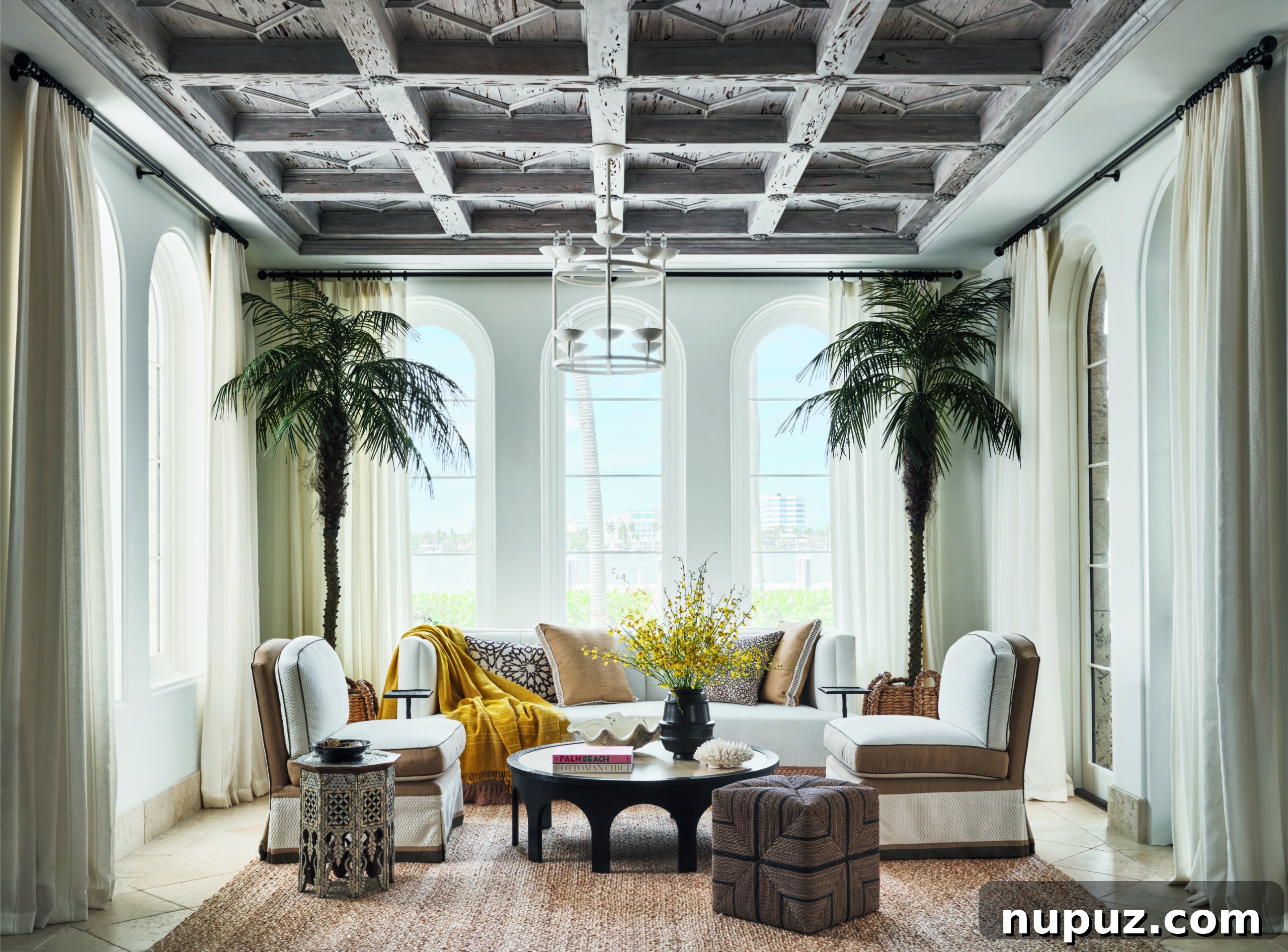 Designing Your Magnificent Life 2 Step inside the world of luxury: A coastal living room with elegant white sofas, a large coffee table, and vibrant green palm trees, showcasing the refined aesthetic of Hilfiger Homes.