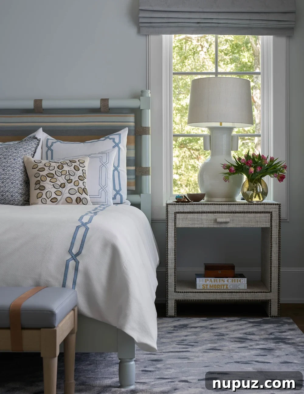 A serene blue and white bedroom features soft, inviting bedding and a stylish nightstand, contributing to a tranquil and elegant classic bedroom design.