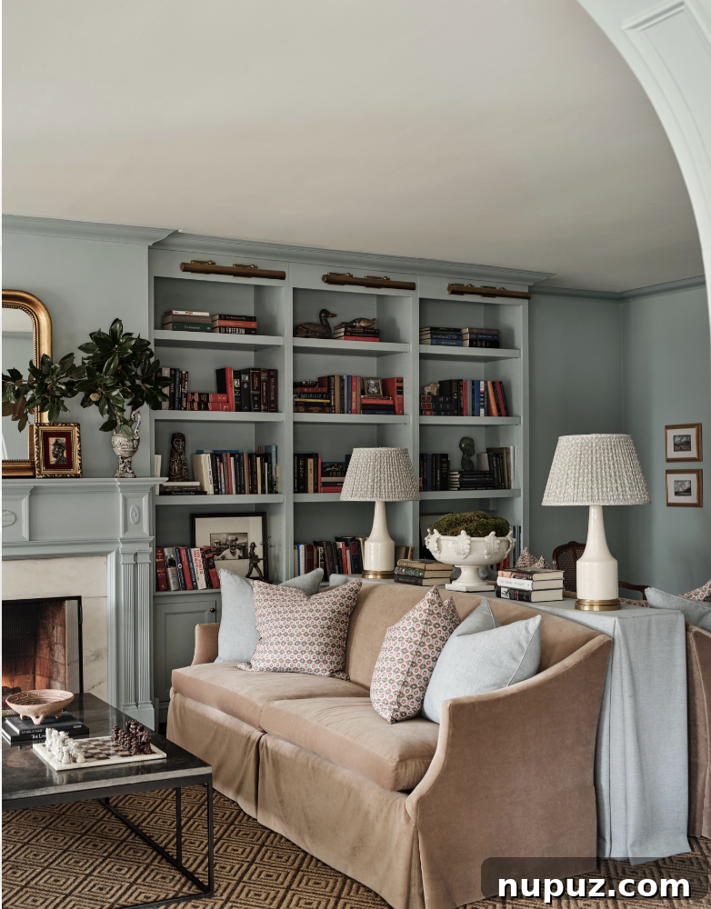 A sophisticated home library featuring Visual Comfort brass library lights and deep, moody blue walls, illustrating a return to rooms with purpose. Interior design by Sabbe Interior Design, photography by Joseph Bradshaw.