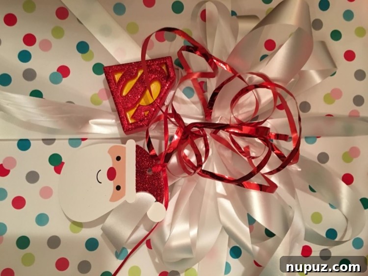 Hallmark Magic: Bringing the Holidays Home 7 A beautifully presented Christmas gift, wrapped in Inspirations from Hallmark paper, adorned with a large bow, a Superman ornament, and a festive Santa gift tag.