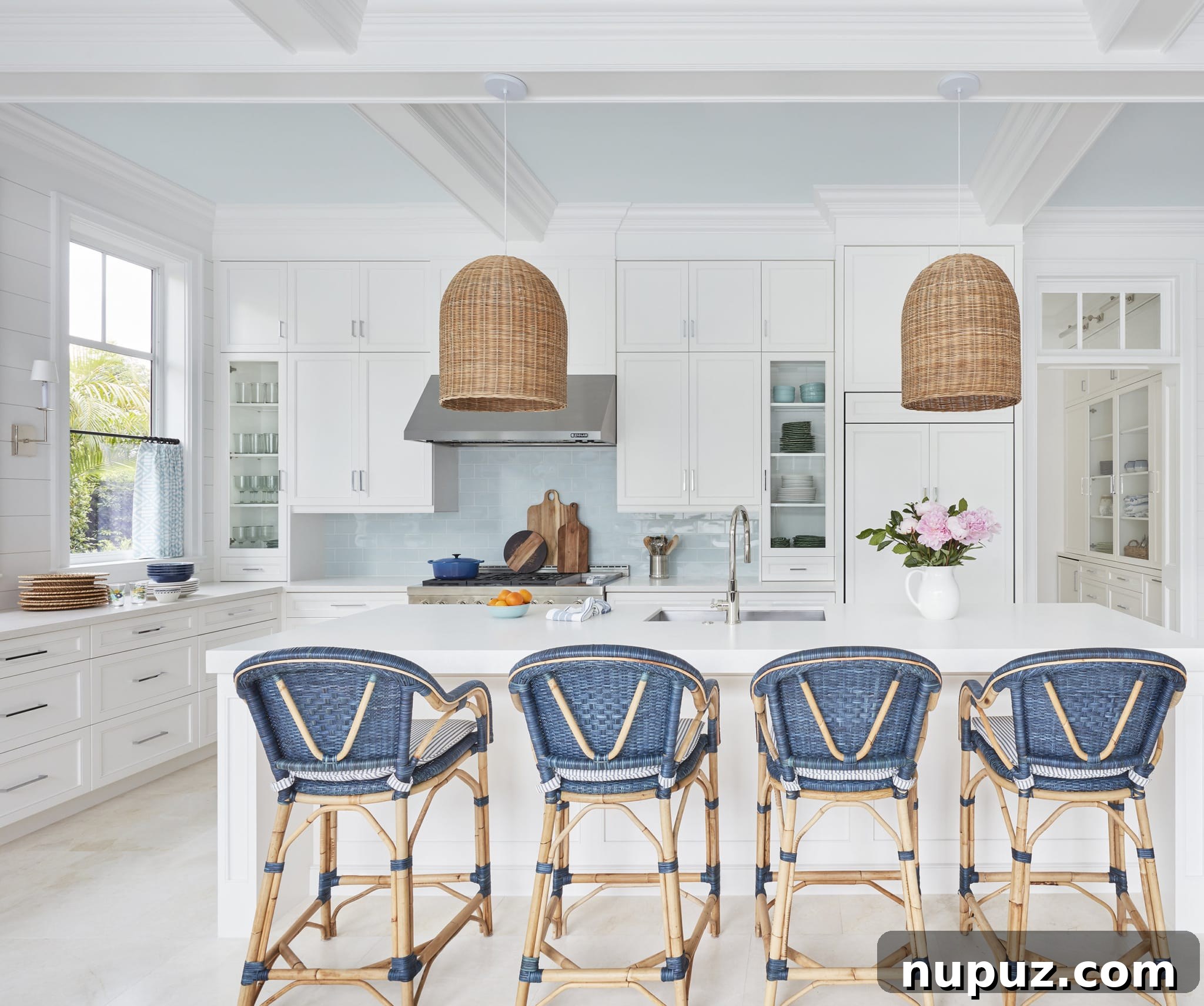 Kara Miller Crafting Kitchens of Unrivaled Beauty 4 A charming and functional Kara Miller kitchen featuring light gray cabinetry, open shelving displaying ceramics, a farmhouse sink, and large windows that flood the space with natural light. The design is both practical and aesthetically pleasing, beautifully captured by Brantley Photography.