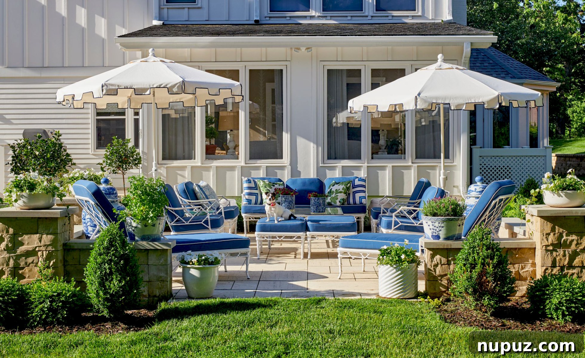 Serene patio with comfortable blue cushions, white umbrellas for shade, and lush greenery, creating a perfect outdoor retreat for morning coffee, designed by Amanda Reynal.