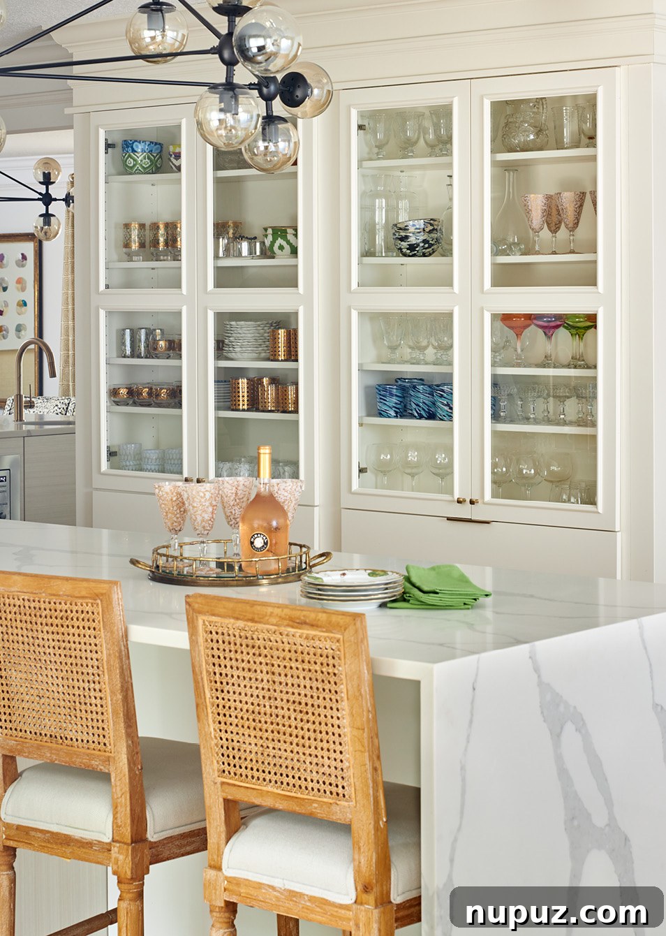 Bright kitchen featuring elegant glass-front cabinets, sophisticated lighting, and a cohesive design by Amanda Reynal for a warm and inviting home.