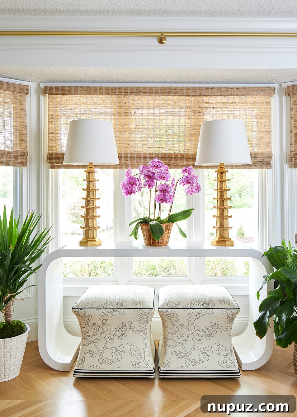 Chic entryway featuring a console table, a pair of elegant lamps, and decorative stools tucked underneath, creating a welcoming and functional space by Amanda Reynal.