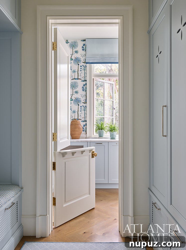 A charming blue and white mudroom in the Sea Island home, complete with a classic Dutch door and exotic palm tree wallpaper, offering both style and utility.