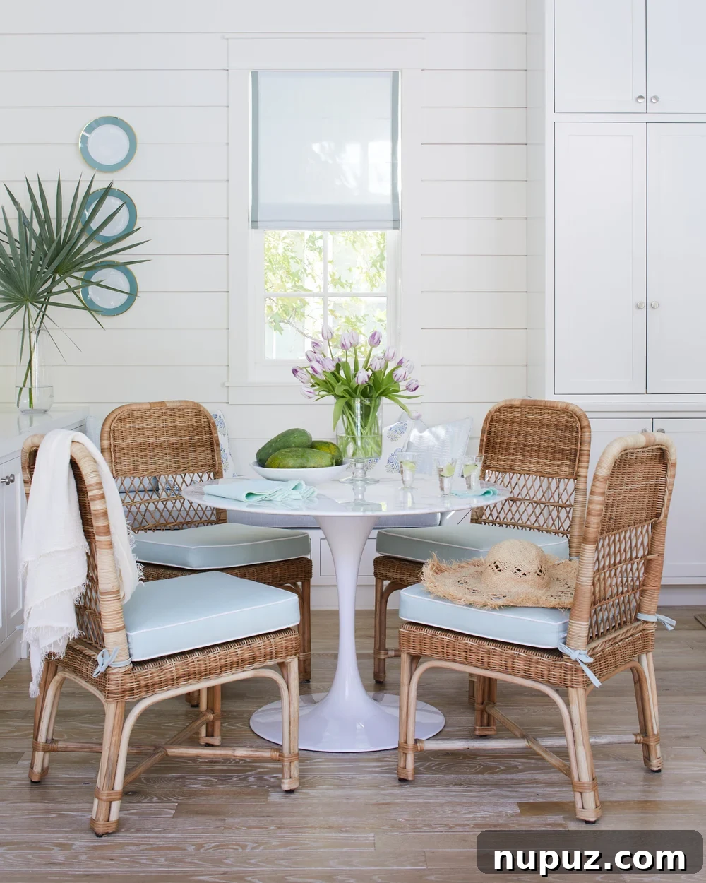 Breezy Blue and White Coastal Bliss 3 Charming breakfast room in a Kara Miller beach house featuring wicker chairs, a round Saarinen dining table, and elegant white paneling, creating a bright and inviting coastal atmosphere.